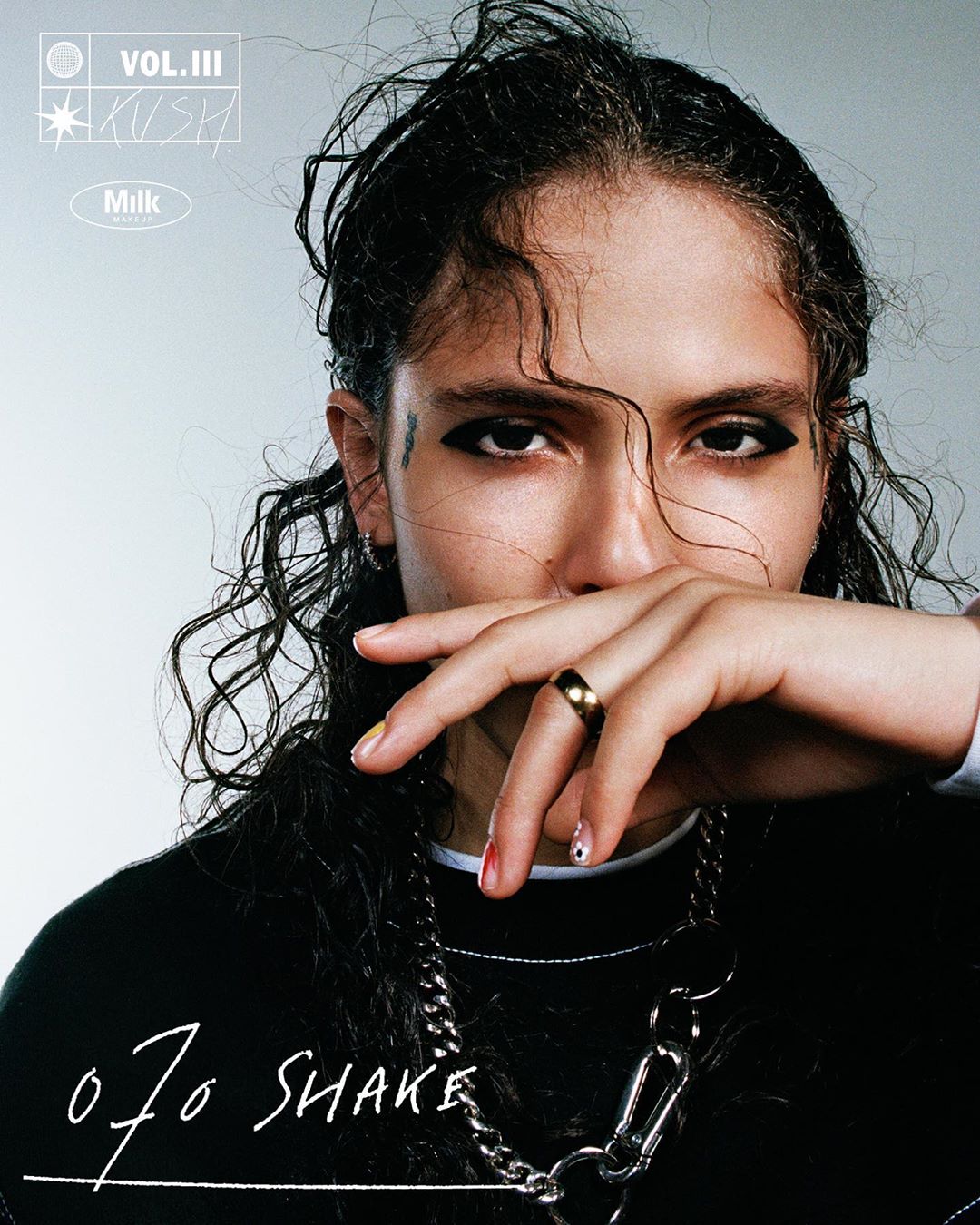Close-up of a young adult with dark curly hair wearing a black sweatshirt and a silver chain necklace, showcasing a modern, edgy aesthetic.
