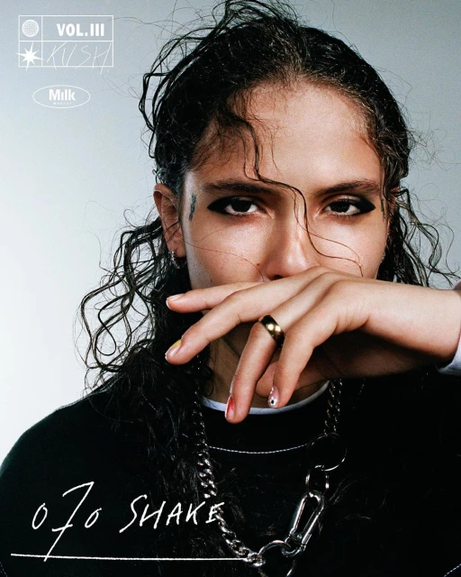 Close-up of a young adult with dark curly hair wearing a black sweatshirt and a silver chain necklace, showcasing a modern, edgy aesthetic.