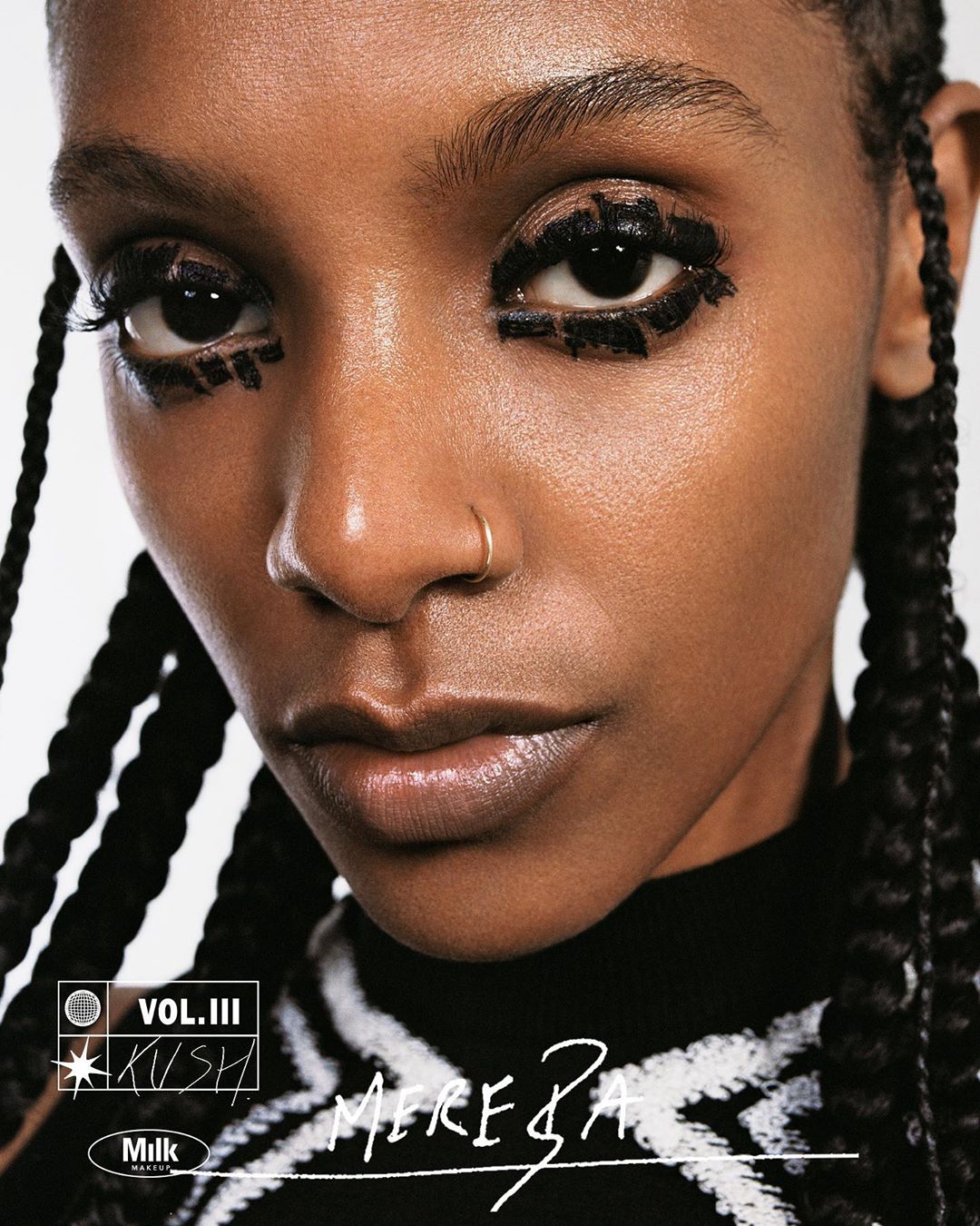 Close-up portrait of a woman with decorative eye makeup and braided hair, wearing a black and white patterned sweater against a white backdrop.
