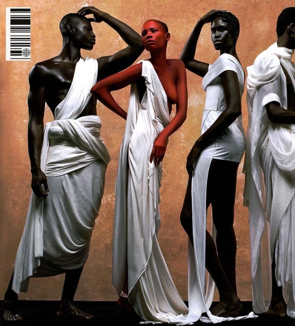 Fashion editorial showcasing a group of dark-skinned models draped in white fabric against a textured neutral backdrop in a studio setting.