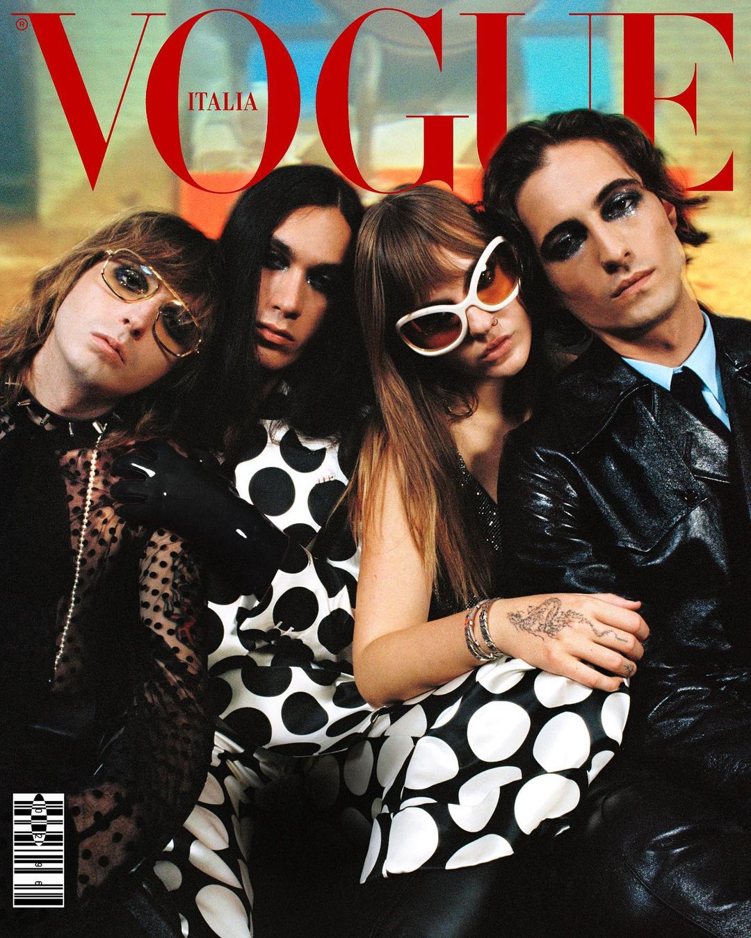 Vogue Italia cover features four people in fashionable clothing, one in a suit, posing indoors with soft lighting and the magazine's logo.