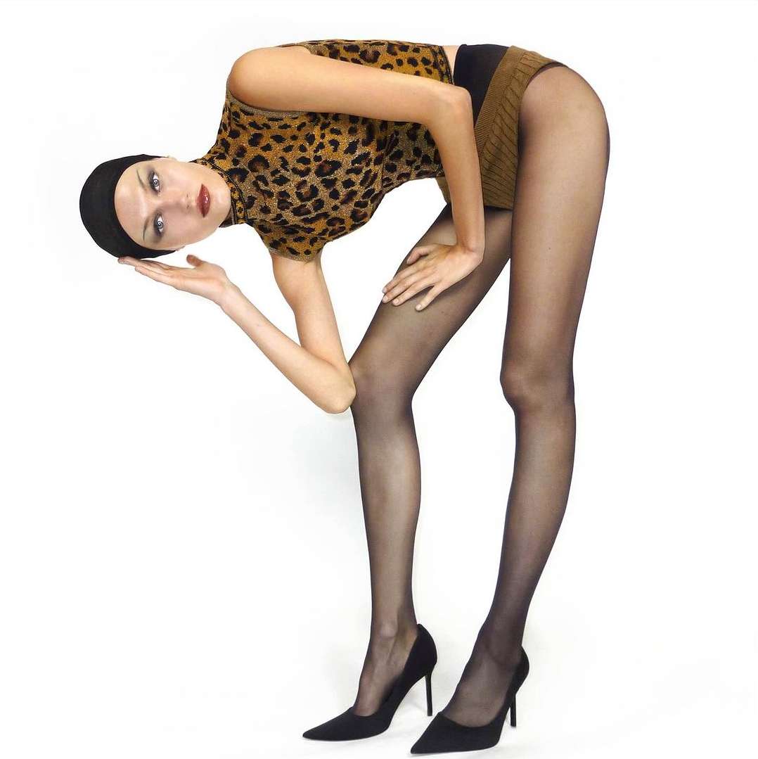 Model in leopard print top and black tights bending forward against a bright white background