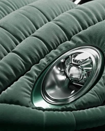 Close-up of a rounded green velvet-covered car body with a polished chrome headlight by Hugo Fournier