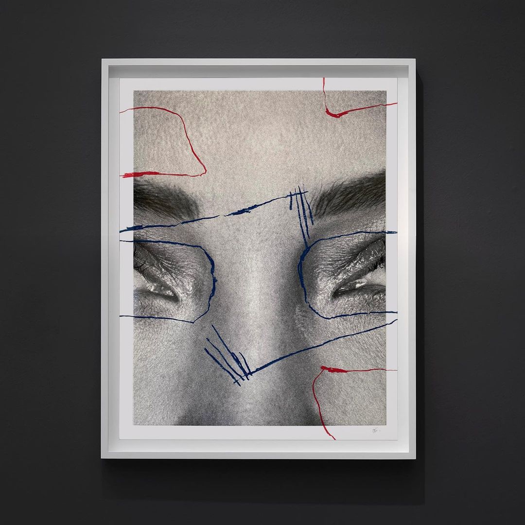 Black-and-white portrait of a woman's face in a white picture frame, enhanced with red and blue graphic lines on a dark wall.