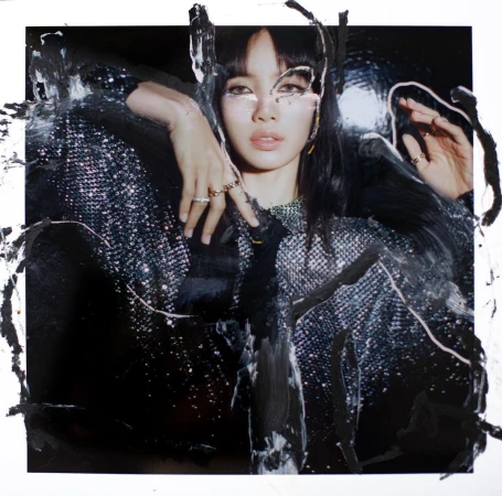 A woman with dark hair in a shiny jacket with paint streaks, fashion photography, studio shot, dark colors, rings and necklace.