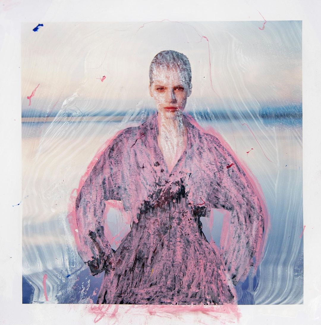 Artistic portrait of a woman with short hair in a pink top against a blurred ocean and sky background, enhanced by a painterly effect.
