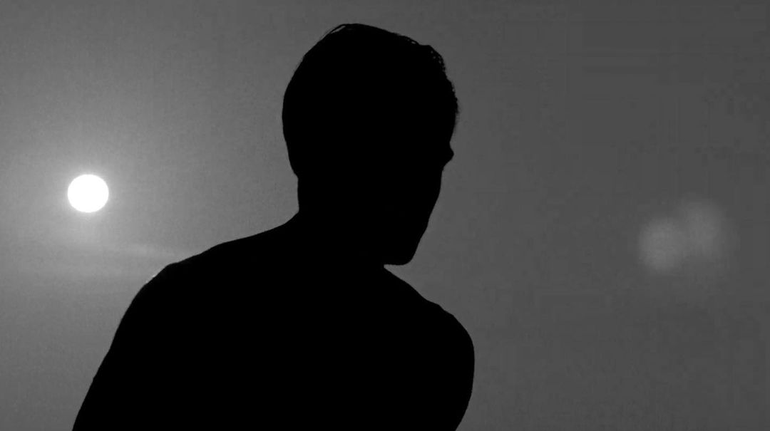 Silhouette of a man against a bright sky with a soft, diffused light source, creating a high-contrast, monochromatic image.