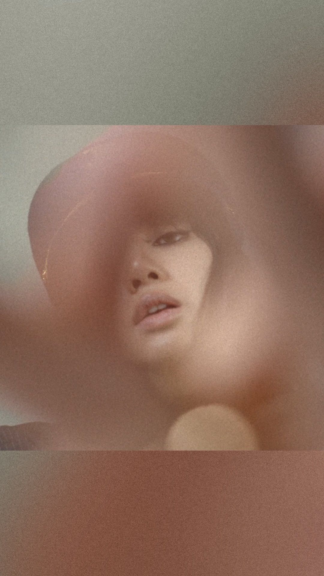 Portrait of a person with light skin wearing a hat, partially obscured by blurry foreground, shot with a low angle and diffused lighting.