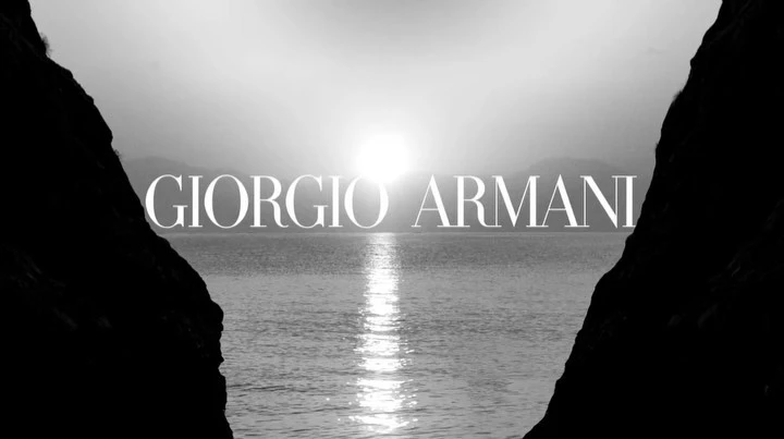 Black and white photo of a sea view framed by dark cliffs, featuring the text 'GIORGIO ARMANI' over the water.