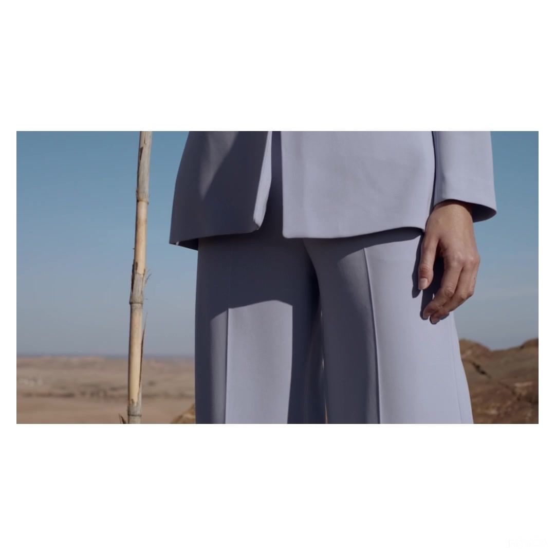 Fashion shot of a woman wearing a light blue suit in an outdoor desert setting with a clear blue sky, captured in a medium shot.