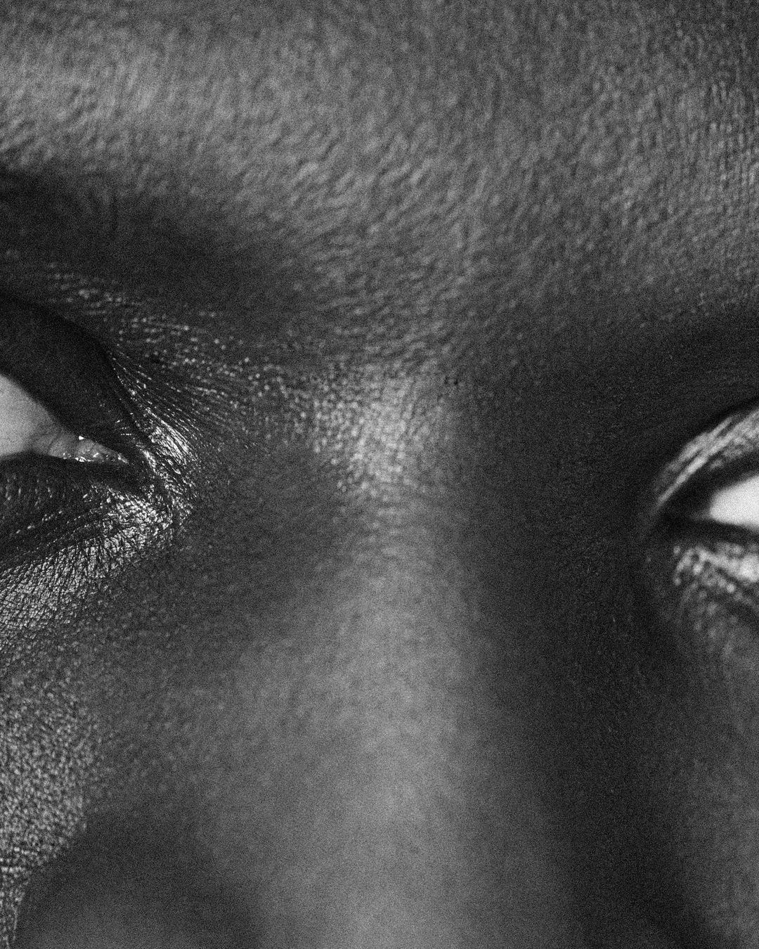 Close-up black and white shot of an African American woman's face featuring her eyes, nose, and forehead with fine skin texture.