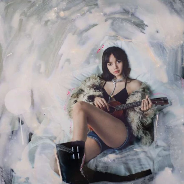 Woman in fur coat sits playing ukulele against a swirled white background, with black boots visible near the image's bottom edge.