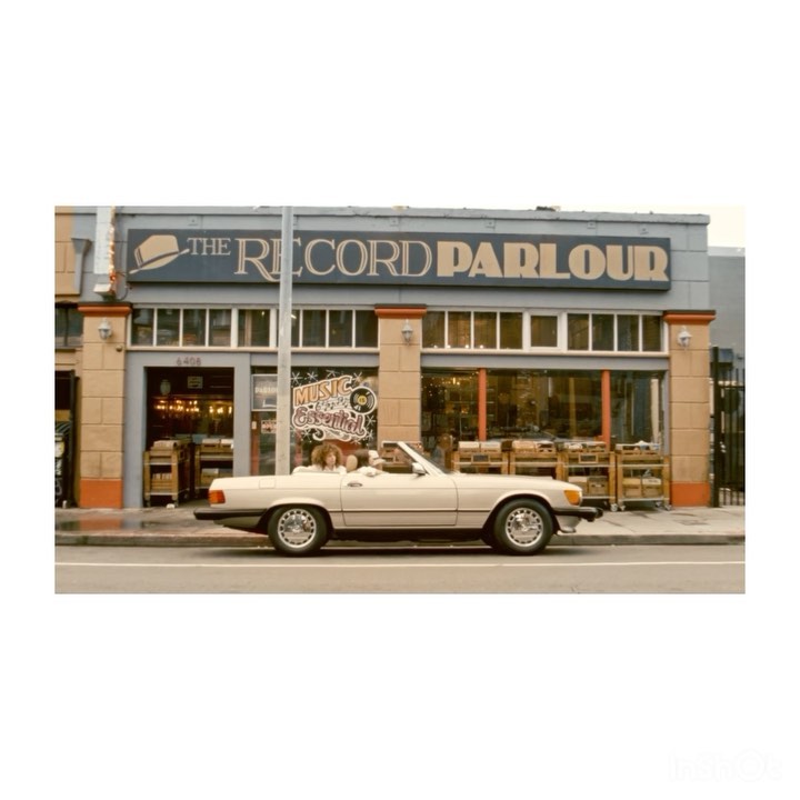 Convertible car parked in front of The Record Parlour store, showcasing the building's exterior, vintage automobile, and signage.