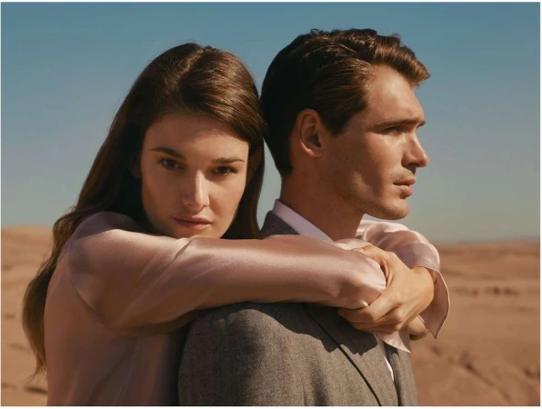 A woman embraces a man from behind against a vast desert landscape under a clear sky.