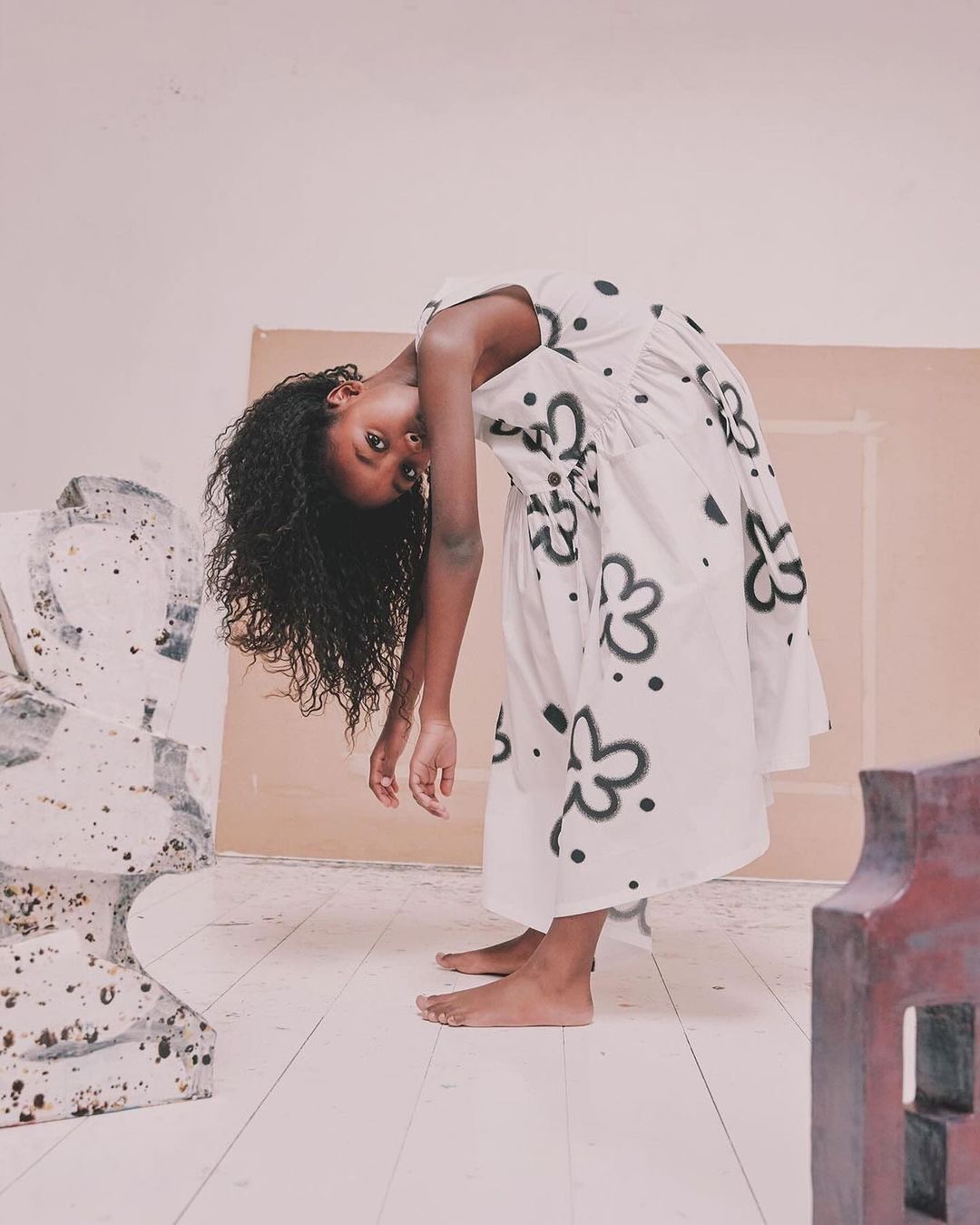 Young black woman in a floral dress bending backwards in a studio setting, showcasing fashion and artistic expression with a unique pose.