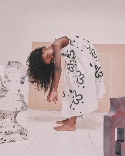 Young black woman in a floral dress bending backwards in a studio setting, showcasing fashion and artistic expression with a unique pose.