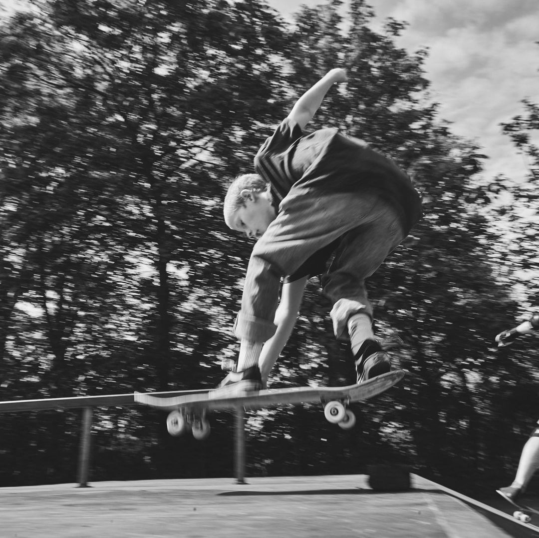 Young skateboarder performing a trick on a ramp in a black and white photograph, trees in the background, motion blur.