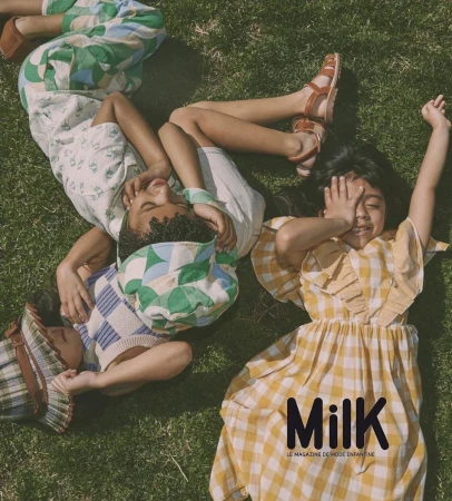 Three smiling children lie on grass in sunlight wearing colourful vintage-style clothes; Milk magazine logo visible at the lower right.