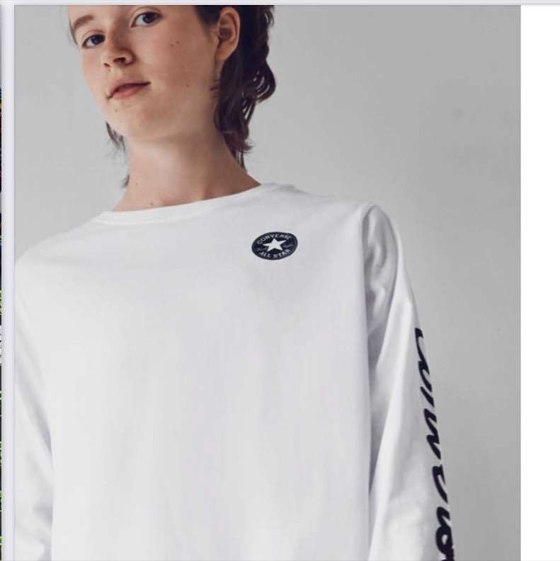 Person in white Converse long-sleeve shirt with logo detail, casual pose against neutral background, studio lighting, close-up.