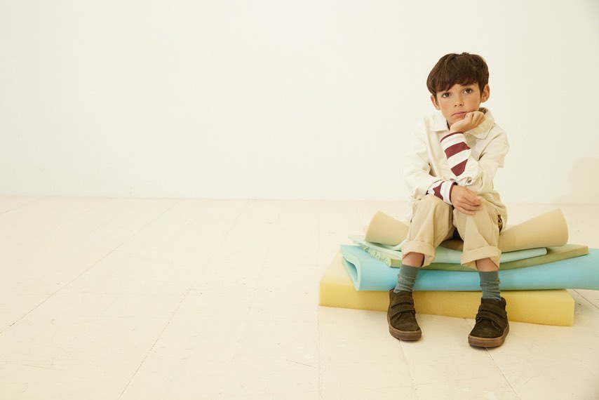 A young child sits on a stack of colorful foam in an indoor setting, looking thoughtfully at the camera with neutral expression.