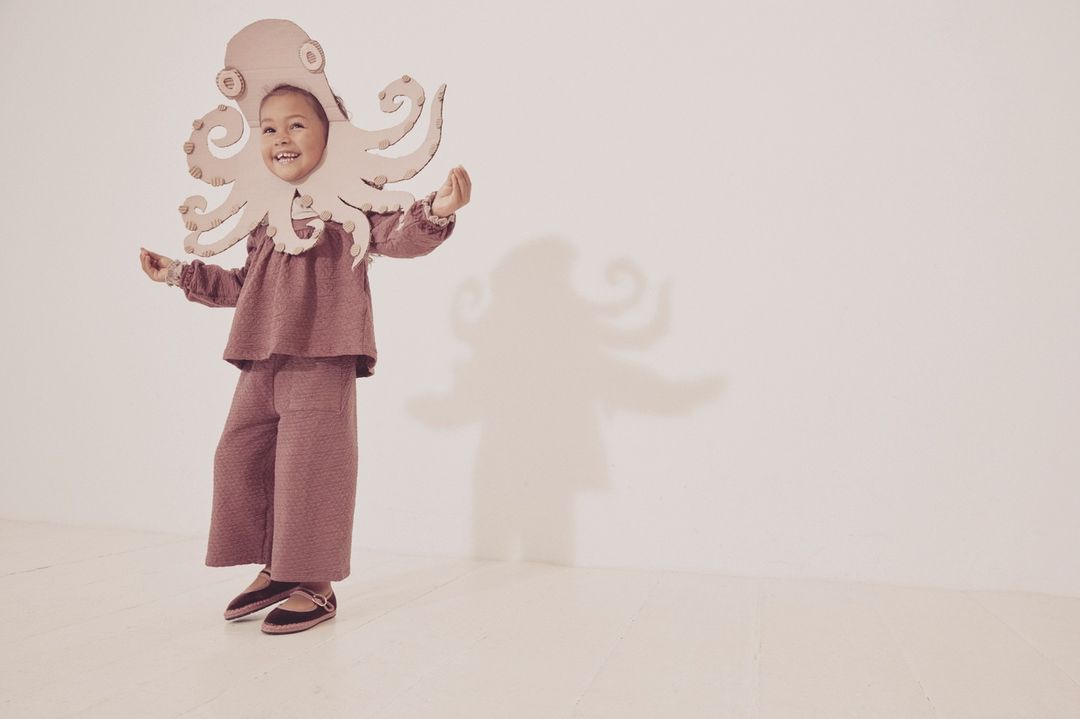 A child in an octopus costume stands in a bright studio with a cheerful expression. The whimsical and playful image evokes a sense of imagination.