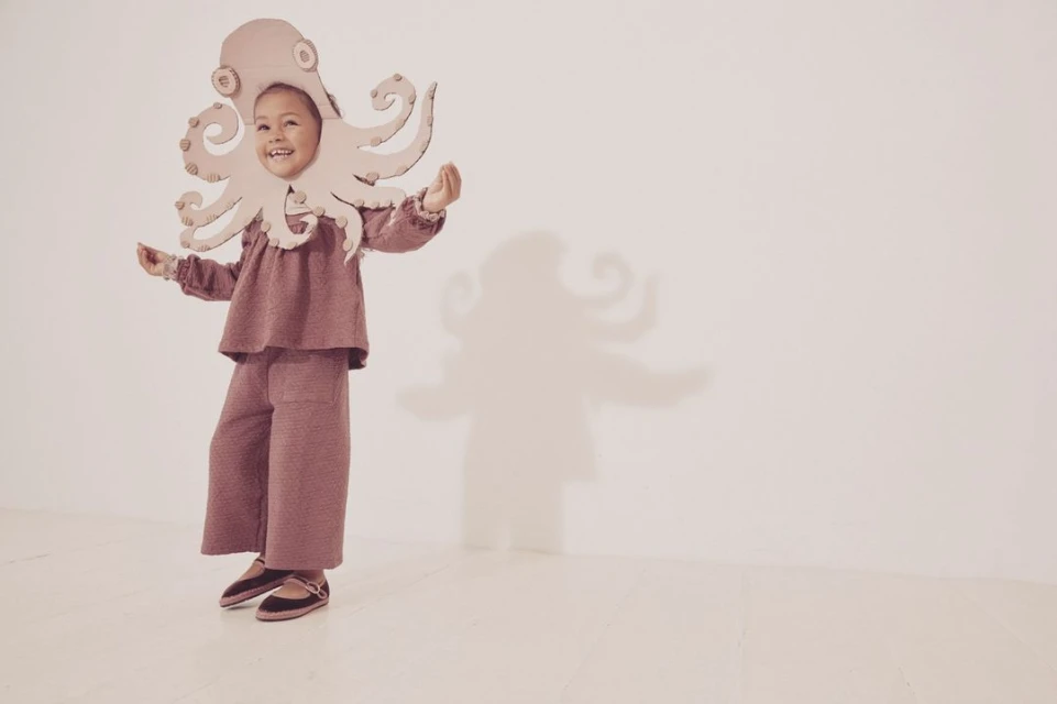 A child in an octopus costume stands in a bright studio with a cheerful expression. The whimsical and playful image evokes a sense of imagination.
