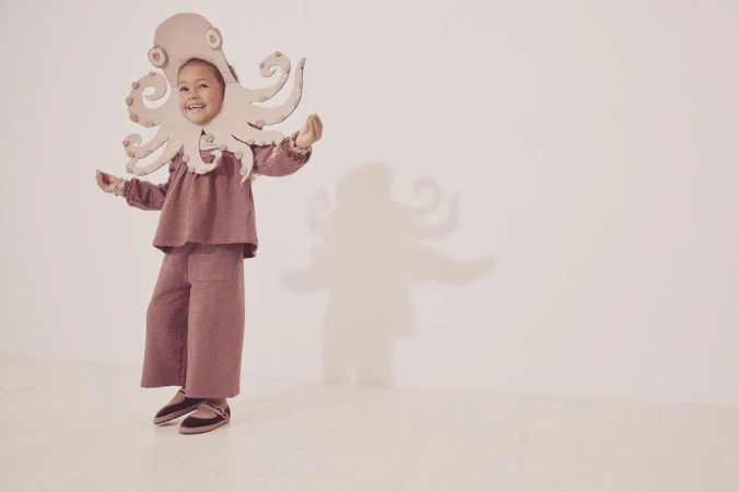 A child in an octopus costume stands in a bright studio with a cheerful expression. The whimsical and playful image evokes a sense of imagination.