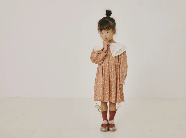 Young child in a patterned dress with a white lace collar standing against a plain white background