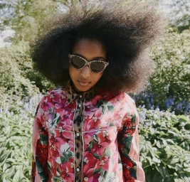 Young woman with voluminous hair wearing animal print sunglasses and a pink floral patterned shirt outdoors