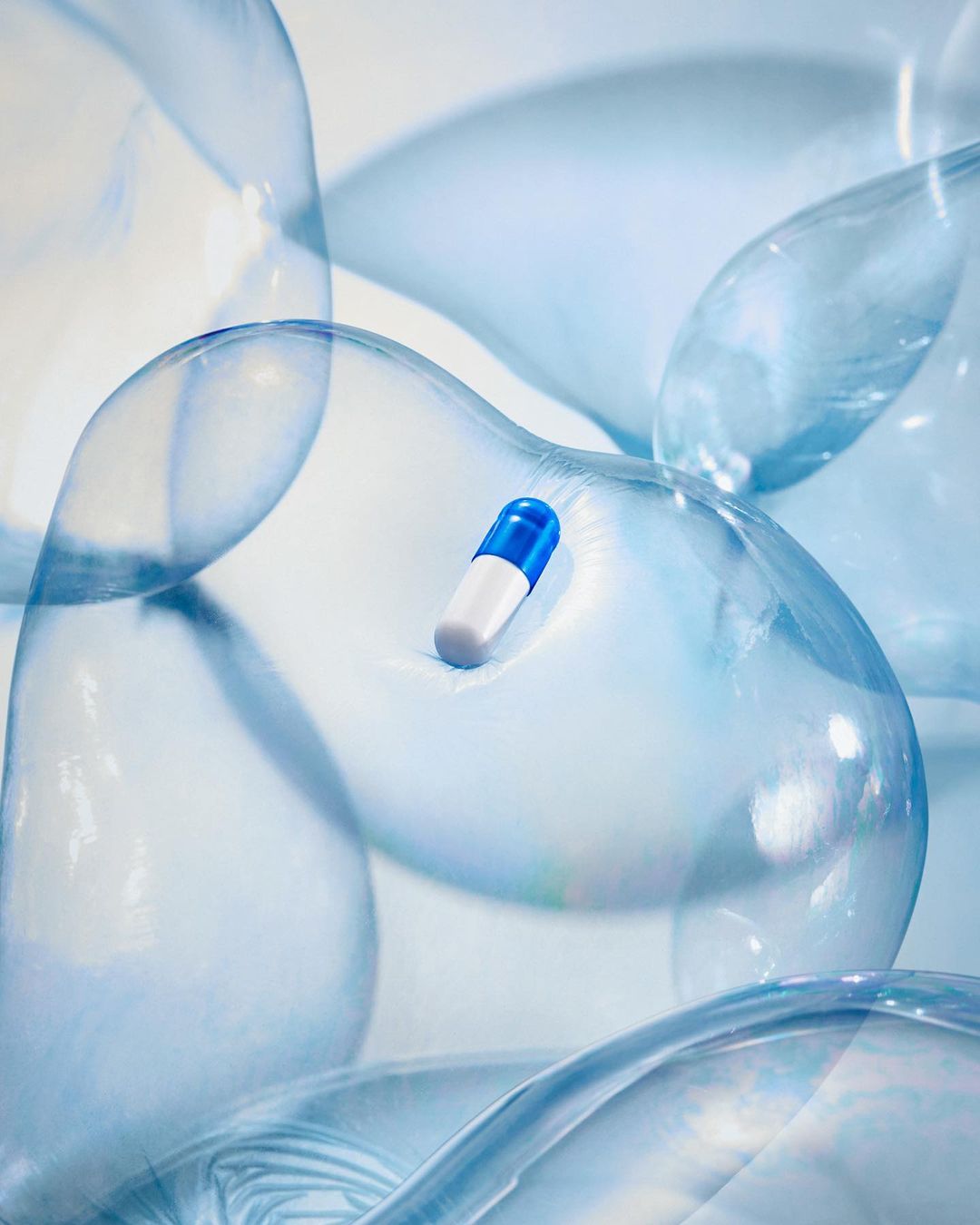 Blue and white capsule pill floating inside a semi-transparent abstract bubble form, set against a soft, blurred background.