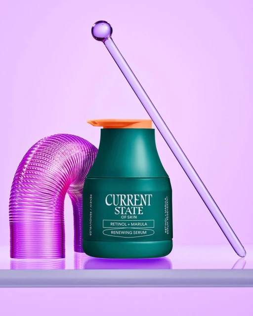 Cosmetic serum bottle stands alongside glass tube and abstract plastic form, set against light purple background for beauty product shot.