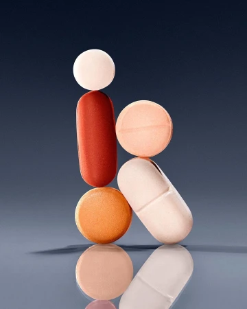Macro photograph of a stacked arrangement of colorful pharmaceutical pills and capsules on a glossy blue surface with subtle studio lighting.