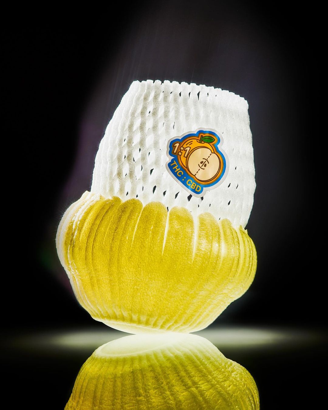 Stylized product shot of a yellow fruit inside a white mesh container with a label, set against a dark backdrop with reflection.