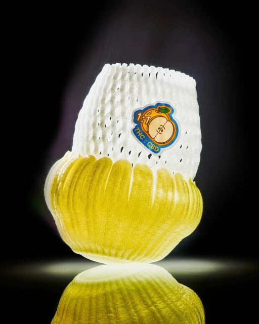Stylized product shot of a yellow fruit inside a white mesh container with a label, set against a dark backdrop with reflection.