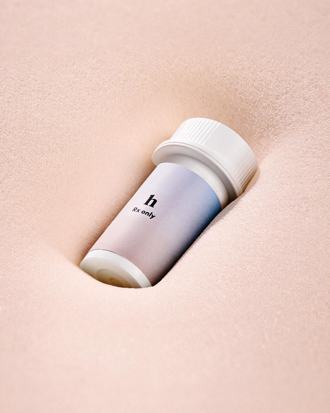 Close-up of a white prescription bottle with a lavender and white label, nestled in soft, textured, pale pink fabric. Studio lighting.