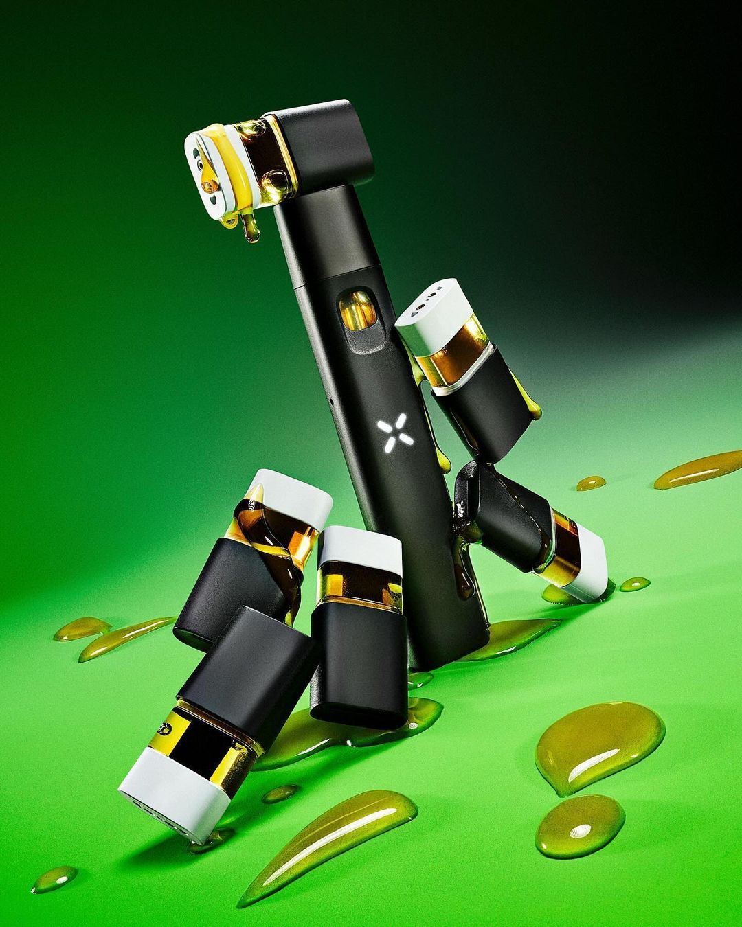 Still life photograph featuring a vaporizer and cartridges with dripping liquid on a green background. Vape and cartridges are arranged artfully.