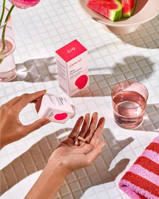 Close-up of a person holding hydration supplements in their palm with the bottle and a glass of water on a tiled surface.