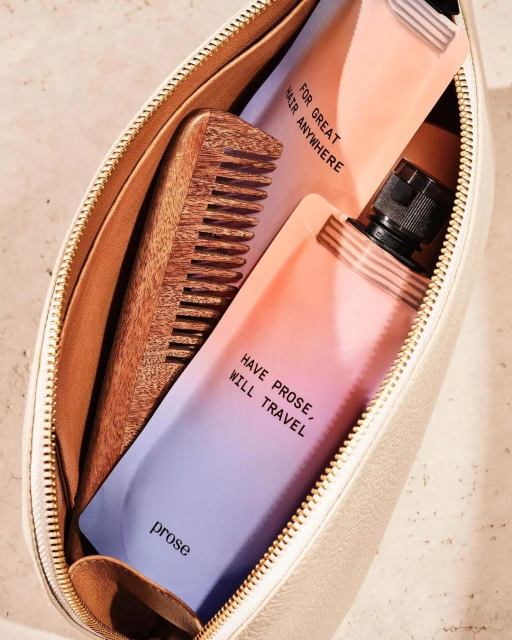 Open toiletry bag with haircare products, including two bottles and a wooden comb, all arranged on a neutral-toned surface.