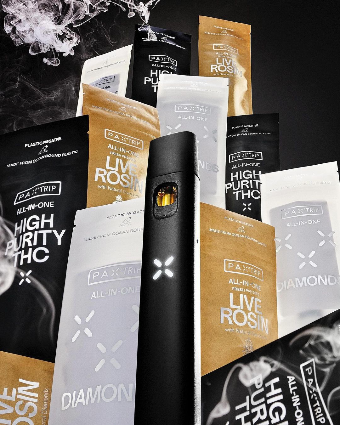 Black vaporizer pen surrounded by Pax Trip all-in-one High Purity THC and Live Rosin product packaging against a black background with smoke.