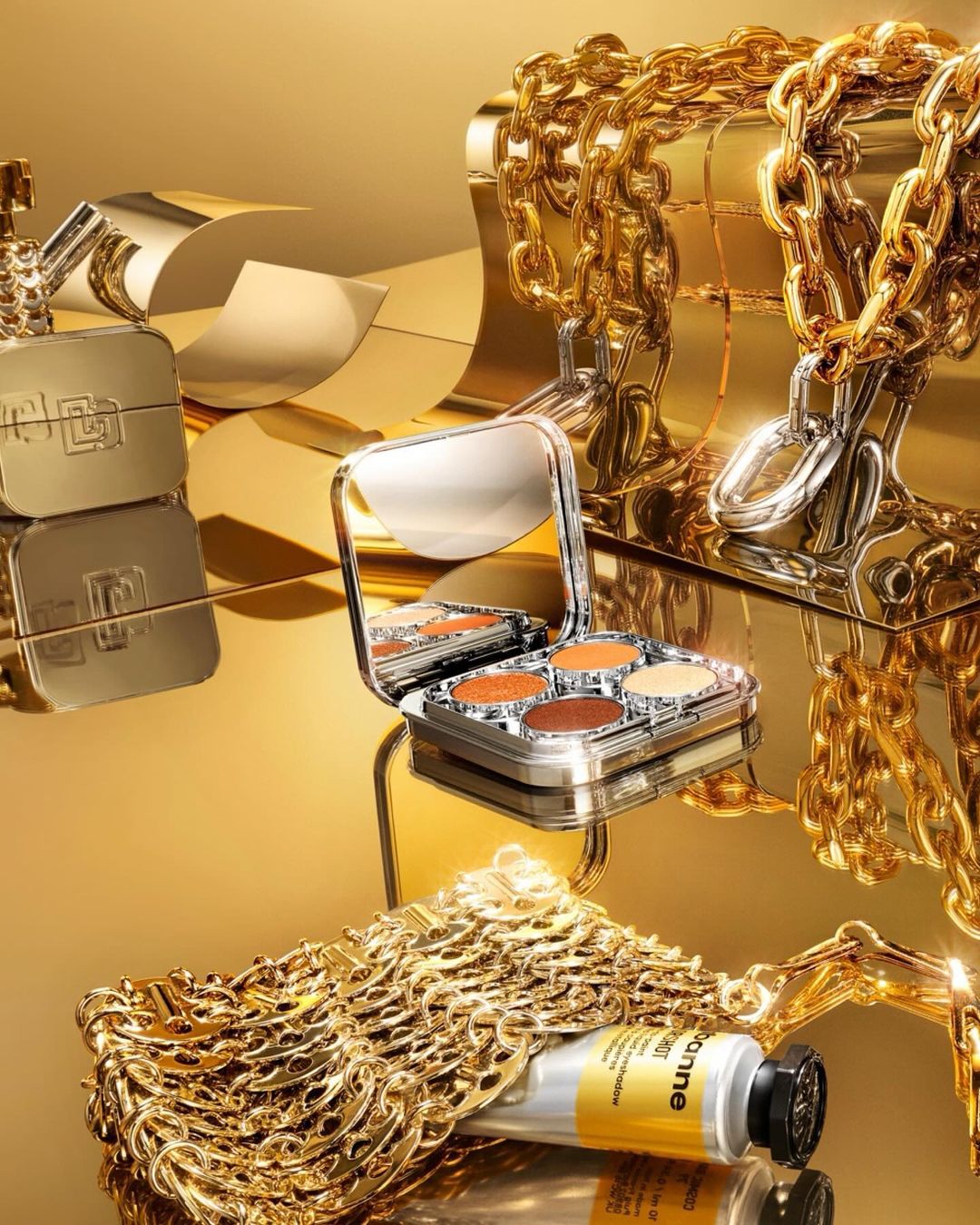 Still life shot of gold-toned makeup compacts, chains, and cosmetic tube; beauty and luxury concept; golden color palette.