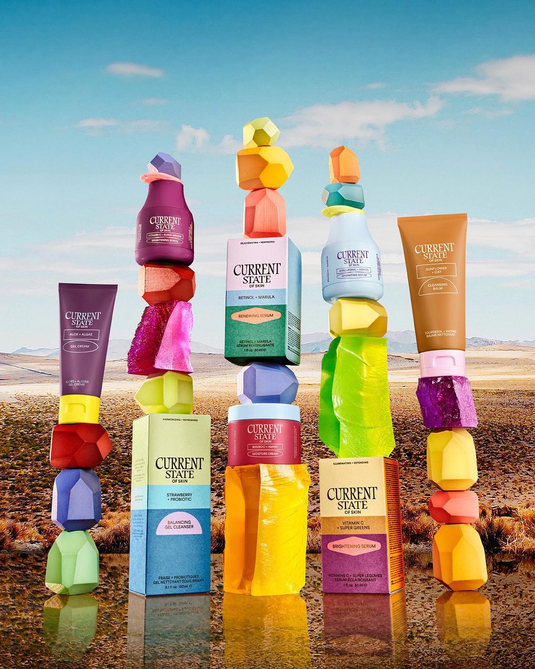 Cosmetic products from Current State are stacked atop one another with crystal-shaped blocks, set against a desert landscape and blue sky.