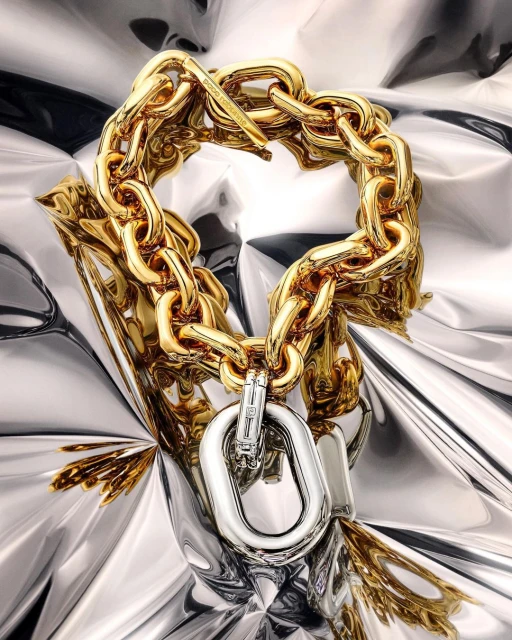 High-fashion jewelry still life: A gold-and-silver chain-link bracelet on silver-colored foil in a studio setting with soft lighting.