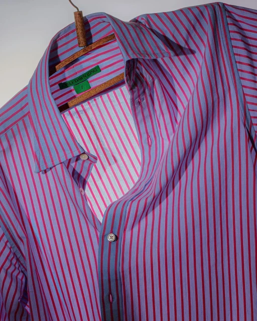 Lavender and magenta striped long-sleeve shirt on a wooden hanger against a light gray background, showcasing fashion apparel.