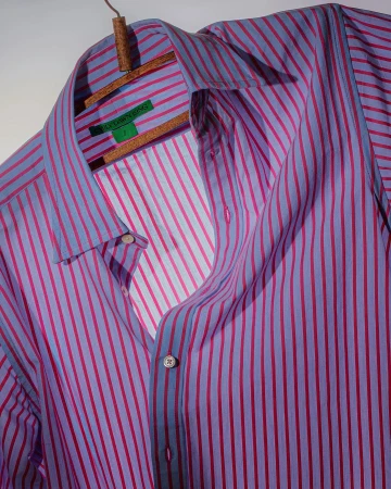 Lavender and magenta striped long-sleeve shirt on a wooden hanger against a light gray background, showcasing fashion apparel.