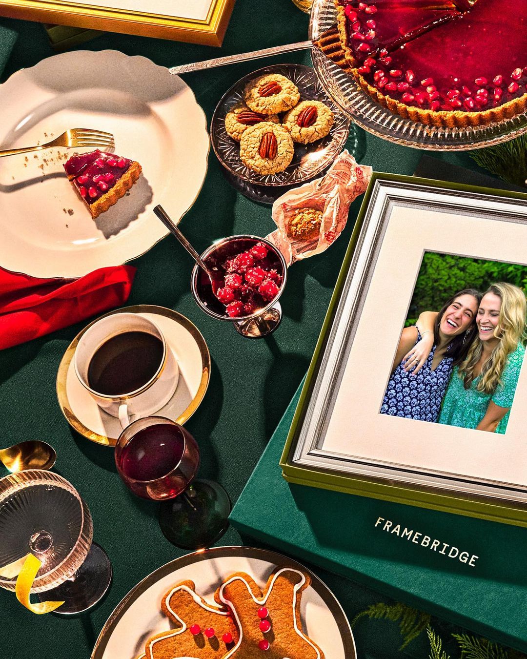 Overhead shot of holiday desserts, a photo frame with two women, and a dark green background, creating a festive and cozy ambiance.