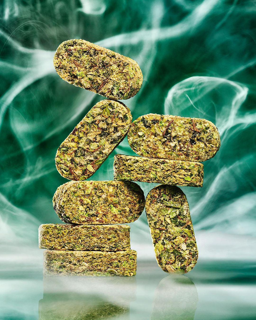 Stacked elongated cannabis edibles create a tower, showcased against an abstract teal and white backdrop for a modern, high-end aesthetic.