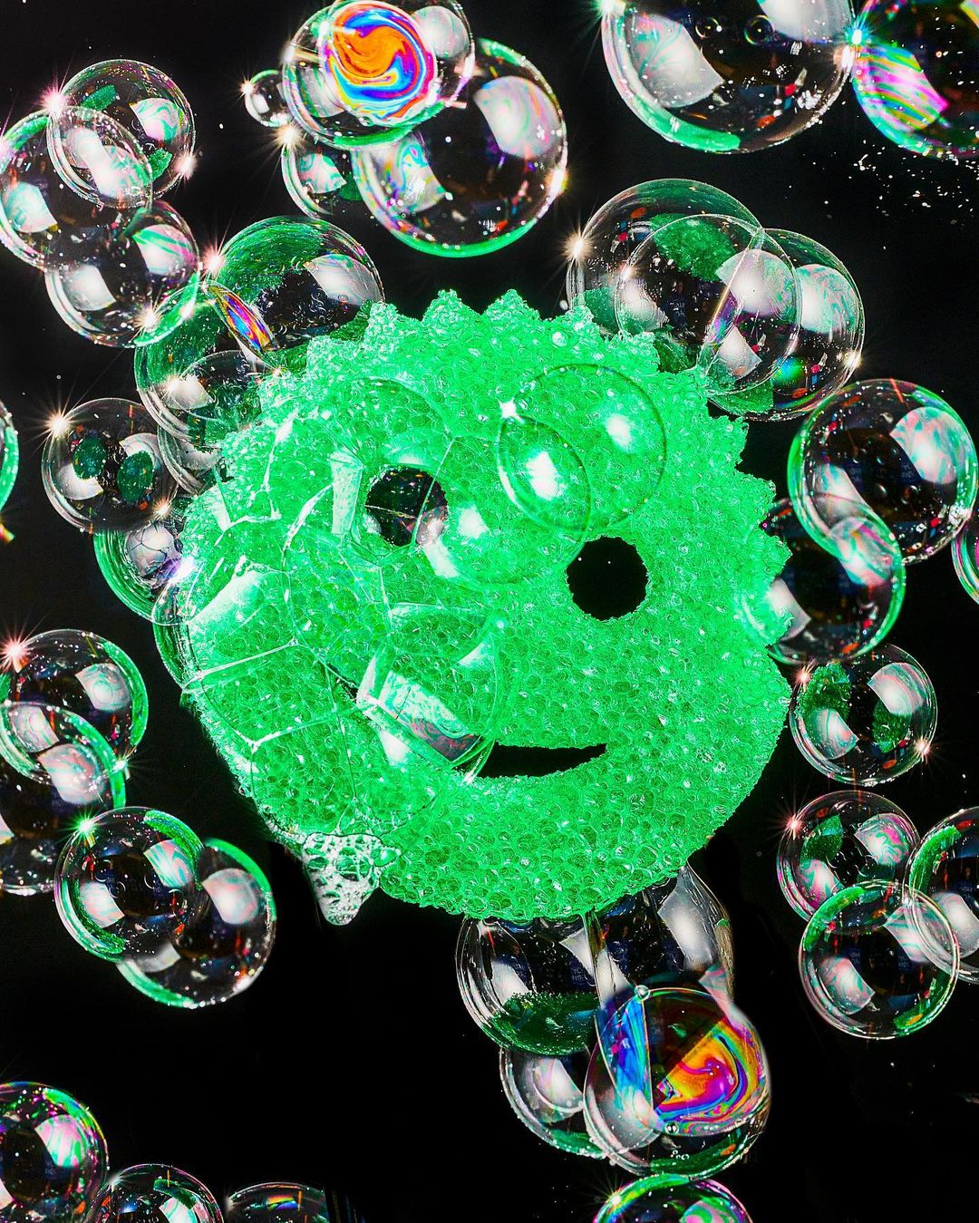 Abstract still life featuring a green textured sphere surrounded by transparent iridescent bubbles floating against a solid black background.