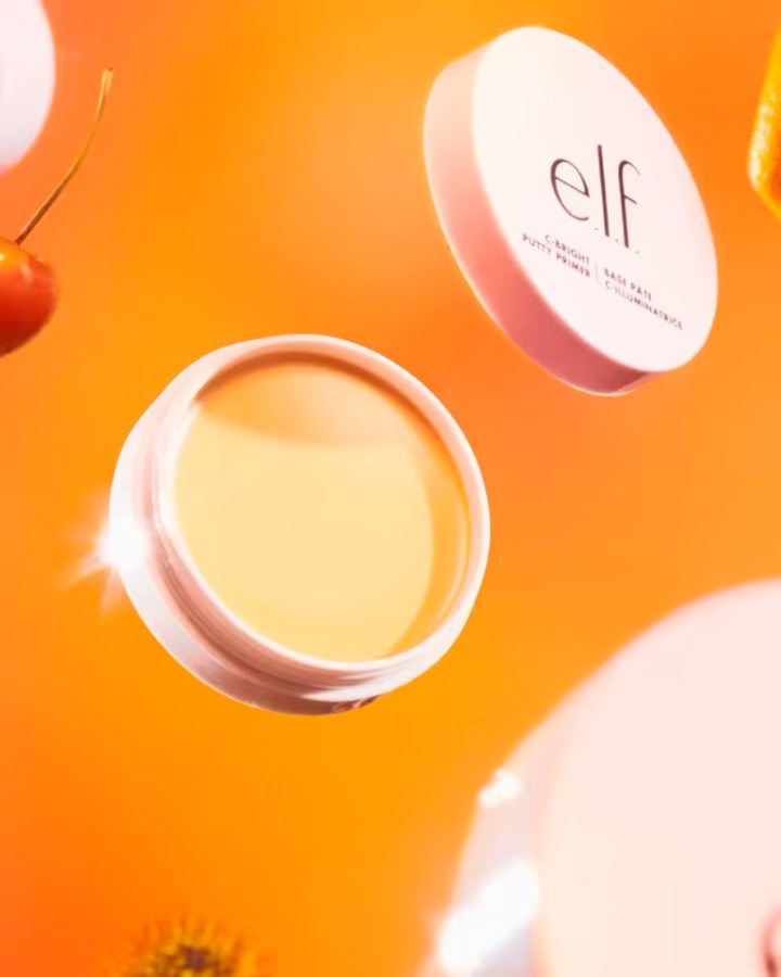 Close-up of e.l.f. C-Bright Putty Primer with surrounding fruit against a bright orange background for beauty product shot.