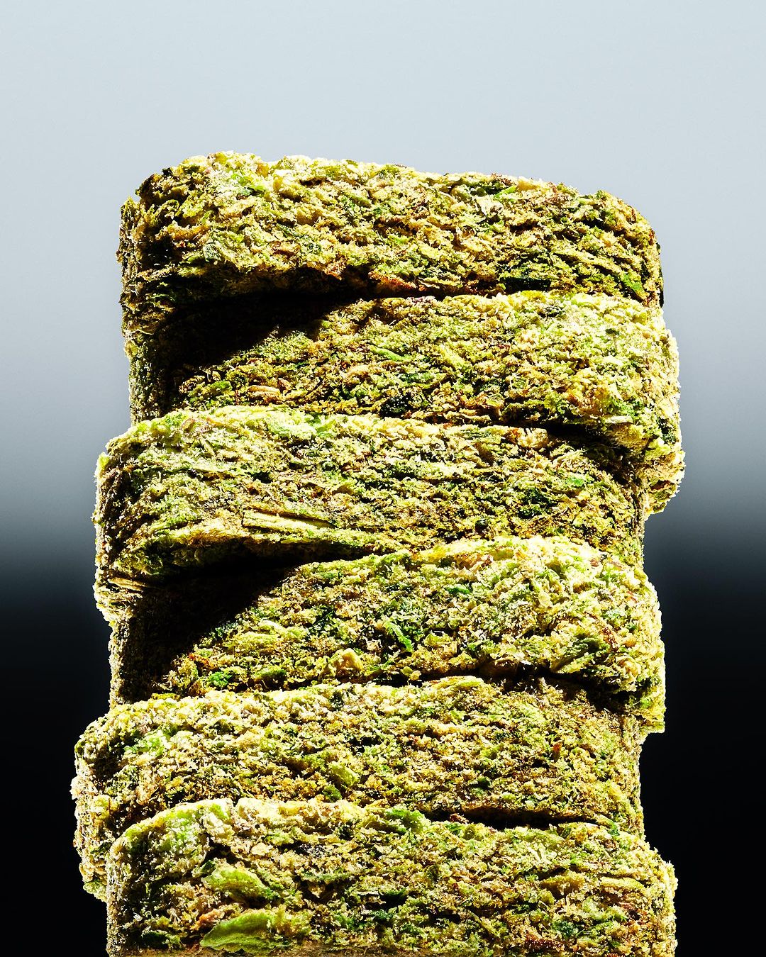 Close-up of stacked hemp material blocks in shades of green and brown, presented against a gradient gray and black background.