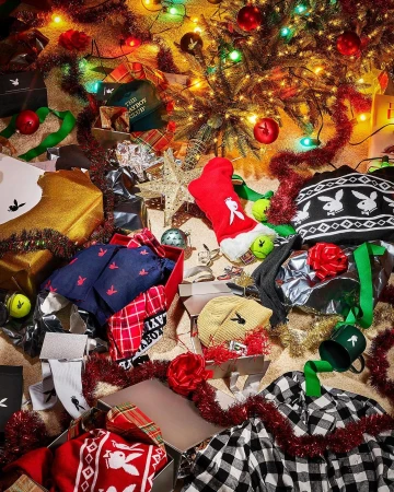 Playboy-themed holiday display with gifts, including apparel, under twinkling Christmas lights and a decorated tree. Presents are open.